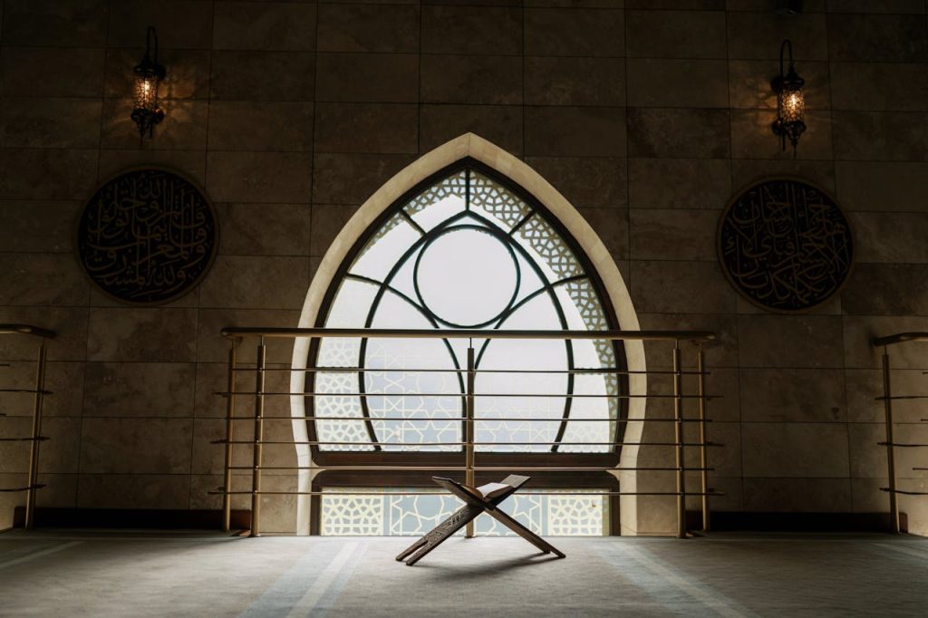 A peaceful mosque interior featuring a backlit window, rehal stand, and intricate architecture.